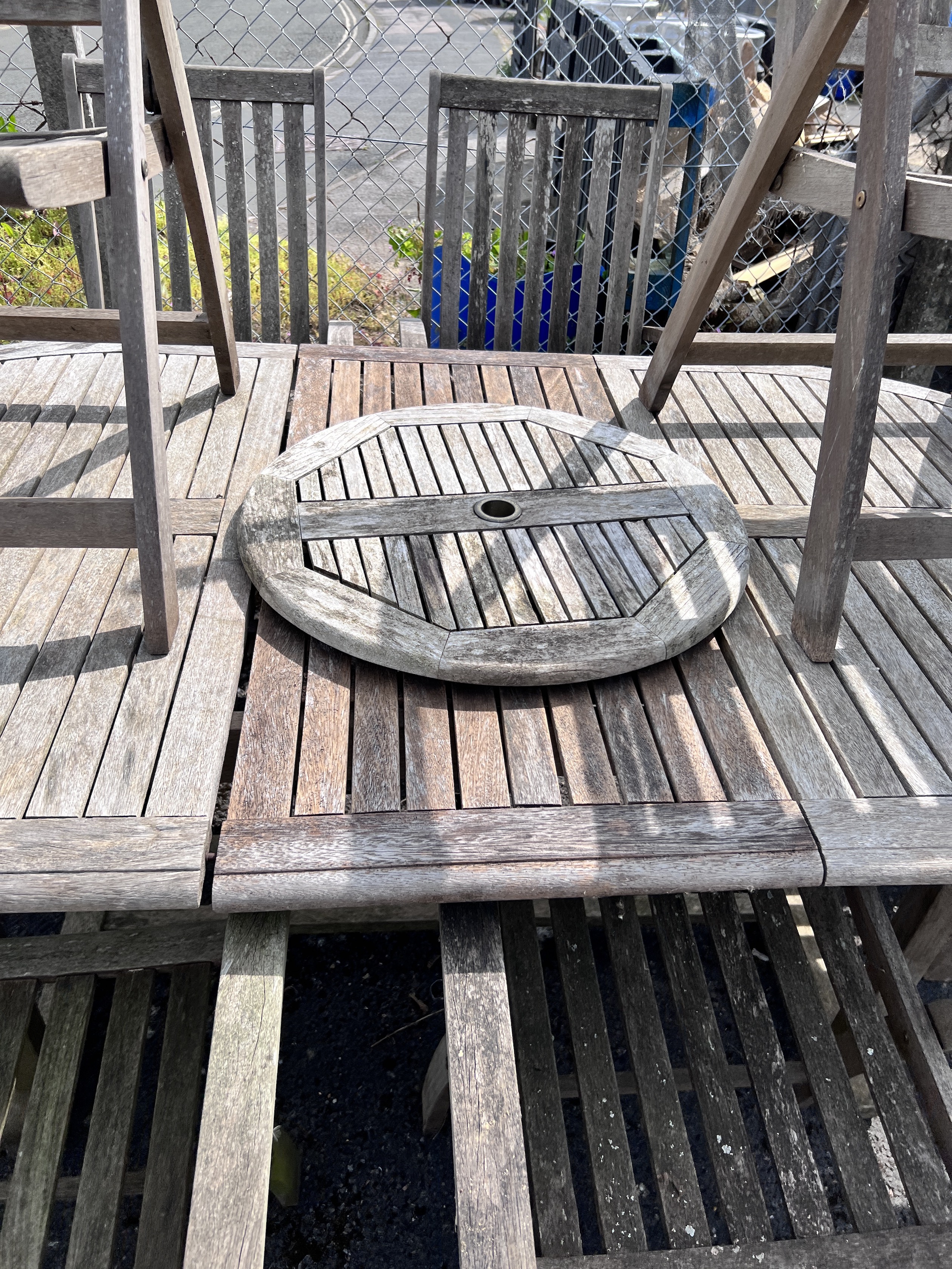 A weathered teak oval extending dining table and eight folding elbow chairs (7 plus 1), table 208cm extended, depth 110cm, height 76cm